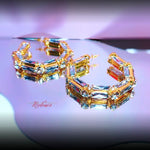 Gold and gemstone hoop earrings on a reflective surface with 'Madam' branding.