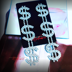 Dollar sign earrings with rhinestones on a black card with 'Madame' branding.
