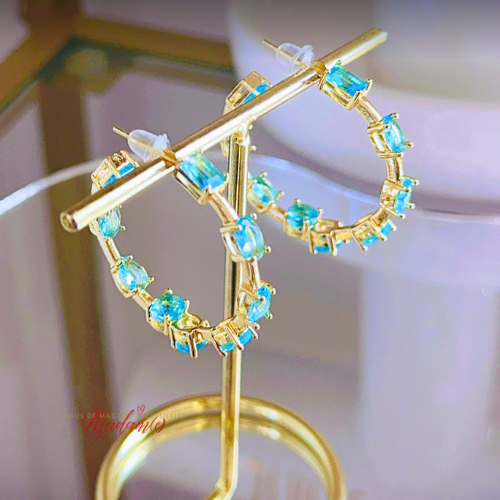 Gold earrings with blue gemstones on a stand against a blurred background