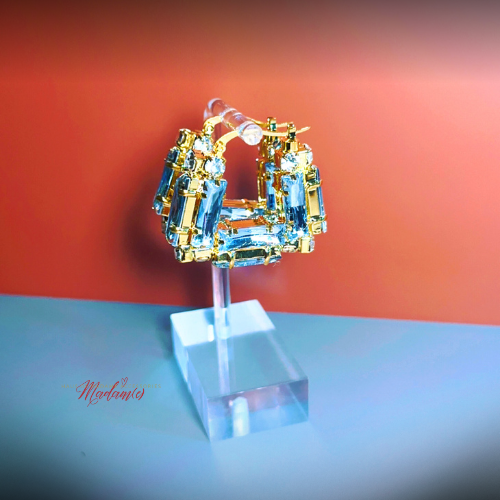 Gold and blue hoop earrings on a clear stand against a gradient background