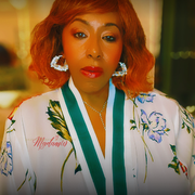 Woman wearing a floral robe with 'Madam' text, indoors.