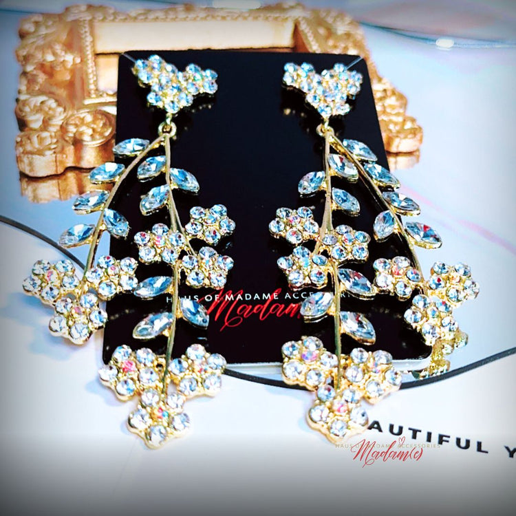 Pair of gold and crystal earrings on a black card with 'Madame' branding.
