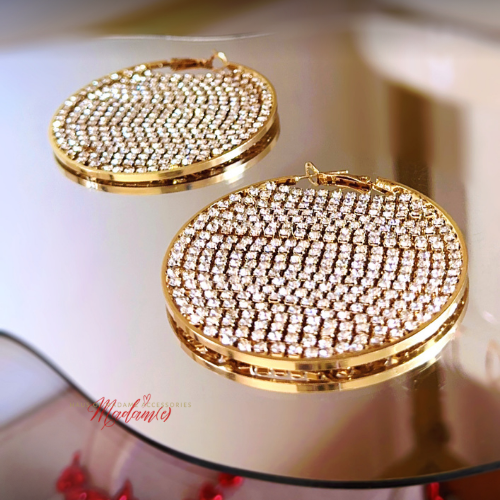 Gold and diamond-studded earrings on a reflective surface