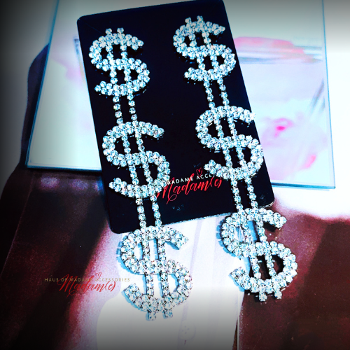 Dollar sign earrings with rhinestones on a black card with 'Madame' branding.