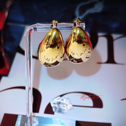 Gold teardrop earrings on a clear stand with a blurred background