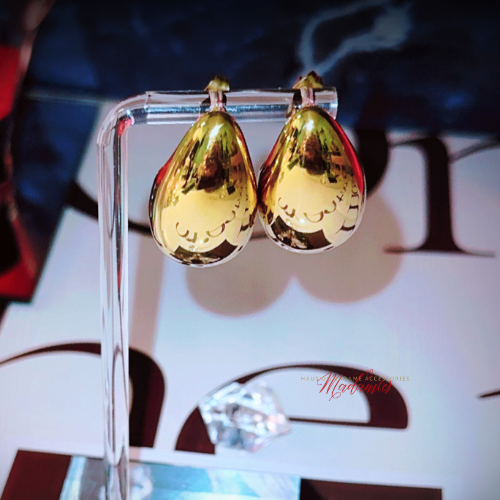 Gold teardrop earrings on a clear stand with a blurred background