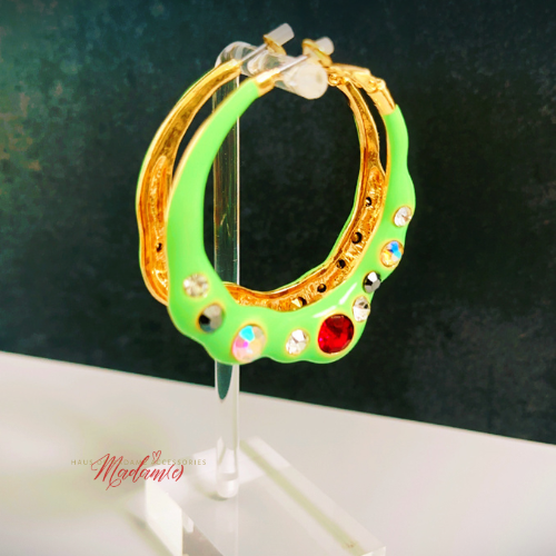 Green hoop earrings with gold accents and colorful stones on a stand against a dark background.