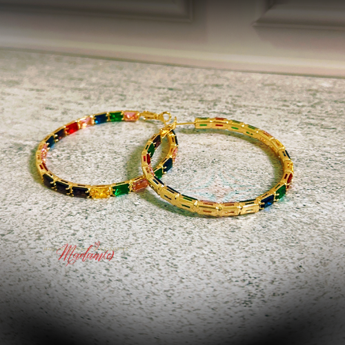 A pair of gold-plated hoop earrings decorated with small rectangular multicolor beads in red, green, blue, and black, resting on a light gray speckled countertop.