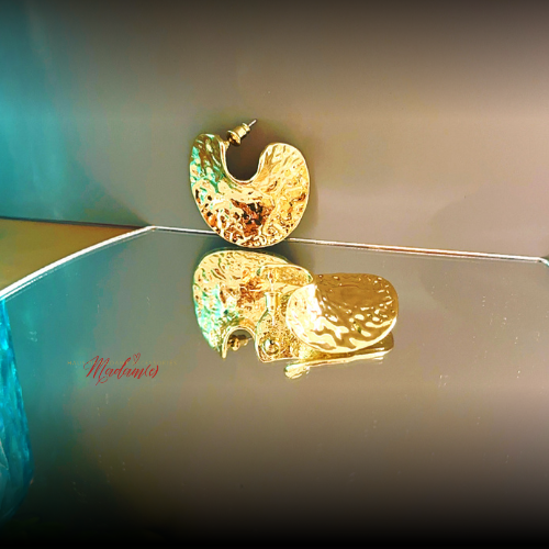 Gold earring on a reflective surface with a blurred background