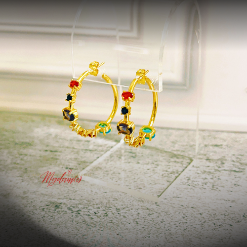 A pair of gold hoop earrings with colorful gemstone accents, displayed on a clear acrylic stand.