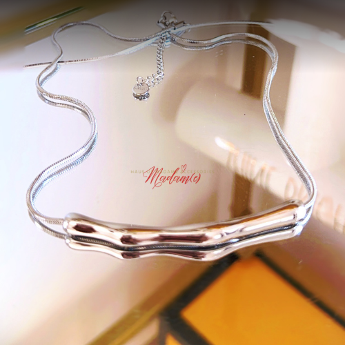 Silver necklace on a reflective surface with 'Madamie' branding.
